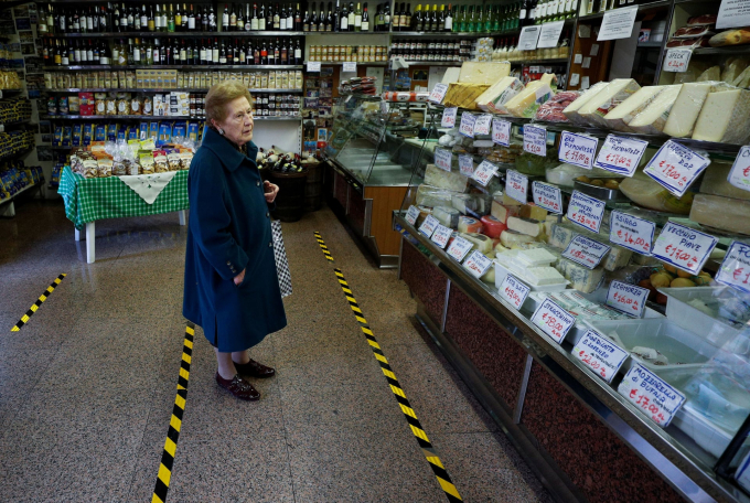 Một phụ nữ đợi mua hàng đằng sau đường kẻ vàng quy định khoảng cách an toàn trong một cửa hàng tạp hóa ở khu vực Trastevere, Rome (Ảnh: Guglielmo Mangiapane/Reuters).