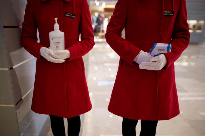 Tại một trung tâm mua sắm, nhân viên cầm một chai dung dịch rửa tay và máy quét thân nhiệt đứng đợ trước cửa ra vào (Ảnh: Reuters/Aly Song).