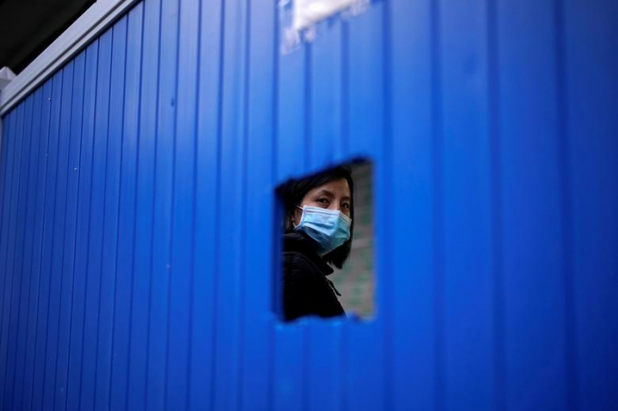 Hình ảnh người phụ nữ đeo khẩu trang được nhìn qua rào chắn ngăn cách khu sinh sống tại Vũ Hán (Ảnh: Reuters/ Aly Song).