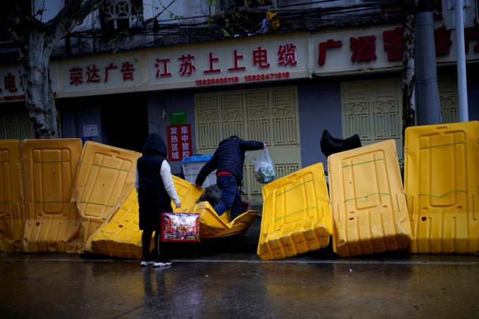 Người dân dẫm bẹp các rào cản được dựng lên để ngăn khu vực nhà ở với đường phố tại Vũ Hán. Để hạn chế sự lây lan, chính quyền đã áp dụng nhiều biện pháp khắt khe để ngăn người dân rời khỏi cũng như đi vào thành phố công nghiệp 11 triệu dân này. Gia đình bị cách ly với người thân, xe công cộng bị tạm dừng và chỉ mở những cửa hàng bán đồ dùng thiết yếu (Ảnh: Reuters/ Aly Song).