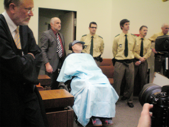 John Demjanjuk bị đưa vào phòng xử án ở Munich vào ngày 30 tháng 11 năm 2009 trong ngày đầu tiên xét xử. Bức ảnh được chụp bởi Thomas Blatt, một người sống sót trong trại tử thần Sobibor. (Ảnh:Thomas Blatt)