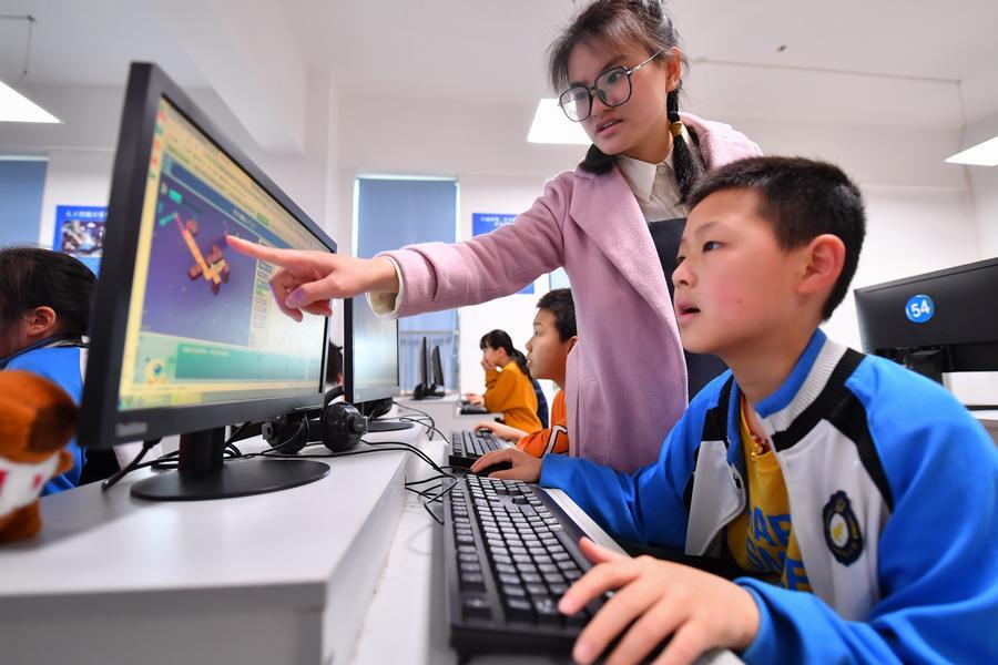 Một giáo viên hướng dẫn học sinh sử dụng máy tính trong lớp lập trình tại một trường tiểu học ở quận Yuhu.
