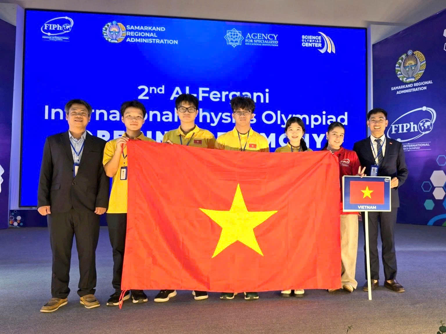 Đoàn học sinh Việt Nam tại FiPhO 2026 (Từ trái qua phải: PGS.TS Phạm Văn Hải, em Trương Bá Chí Thành, em Lê Bá Tuấn Việt, em Tăng Hạo Nhiên, em Lê Hồng Nhân, tình nguyện viên và PGS.TS Nguyễn Công Toản).